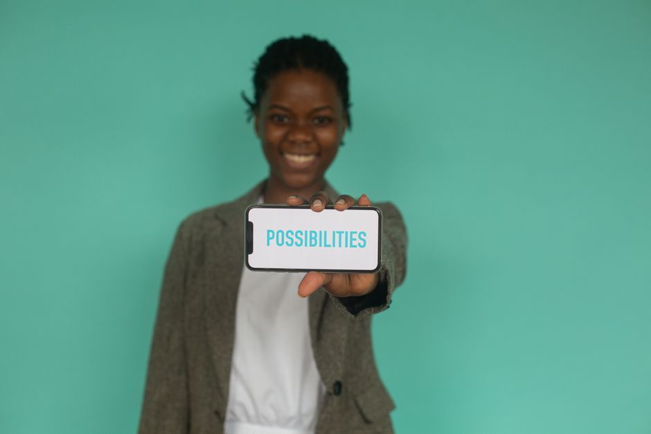 A smiling woman presents a smartphone with 'Possibilities' on the screen, encouraging optimism.