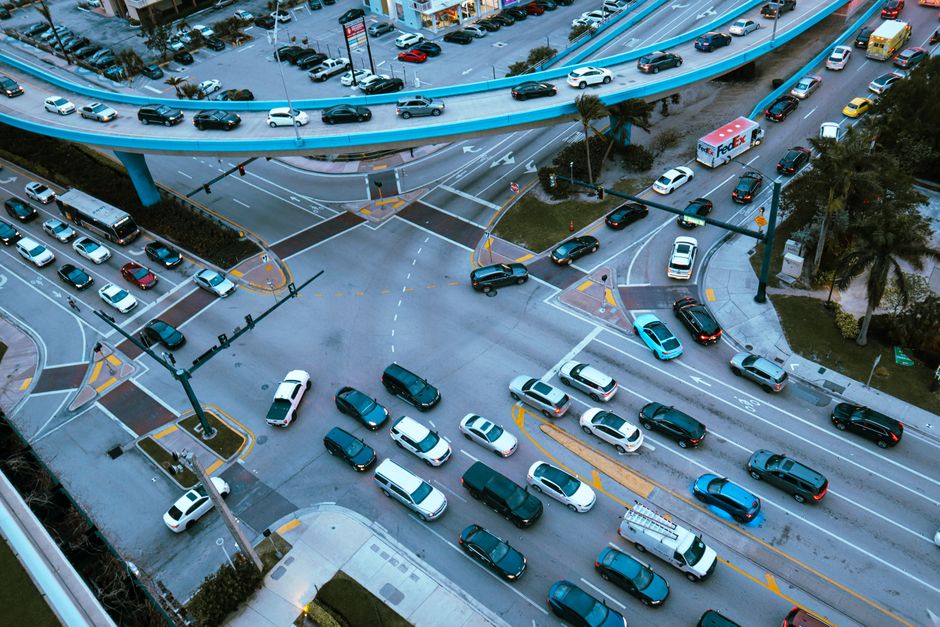 Aerial view of a busy urban intersection filled with cars and traffic under a blue overpass.