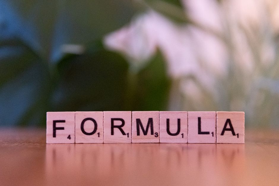 Close-up of Scrabble tiles spelling 'Formula' on a wooden surface with a blurred background.
