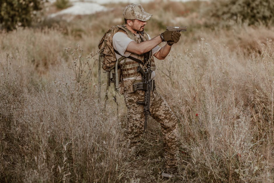 A camouflaged soldier aiming a weapon in a grassy field, ready for action.