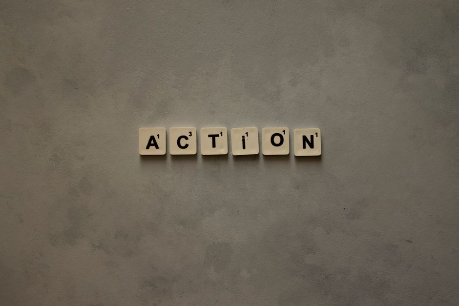 Scrabble tiles forming the word 'Action' on a textured gray surface, conveying motivation.