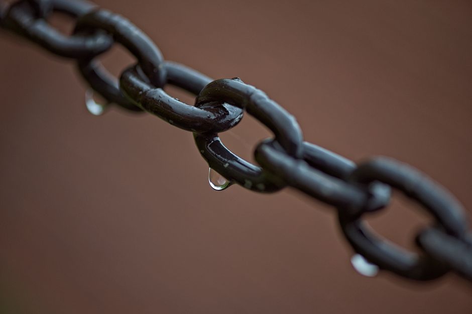 Macro shot of metal chain links with raindrops, showcasing texture and moisture.