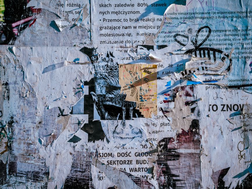 Close-up of a textured wall with layered and peeling posters, showing diverse colors.