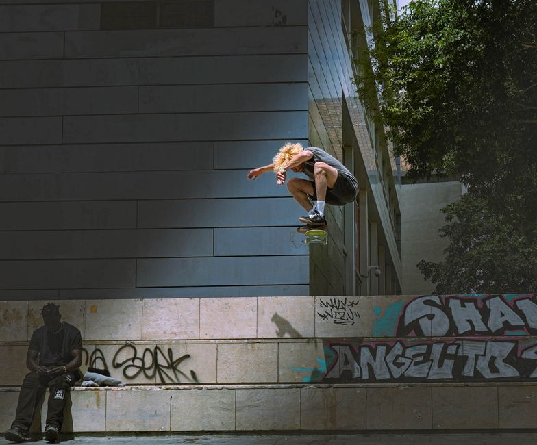 Skateboarder mid-air in Barcelona urban setting with street art and architecture.