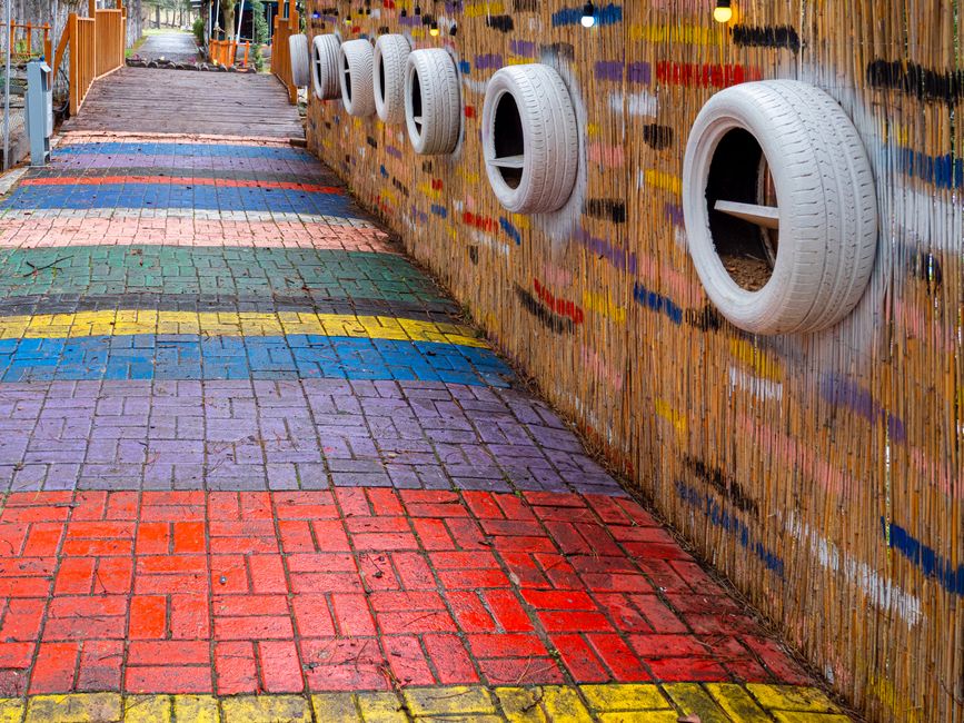 A vibrant walkway with colorful bricks and artistic wall made from recycled tires.