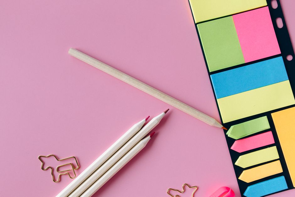 Colorful stationery including pencils and sticky notes on a pink surface, ideal for educational themes.