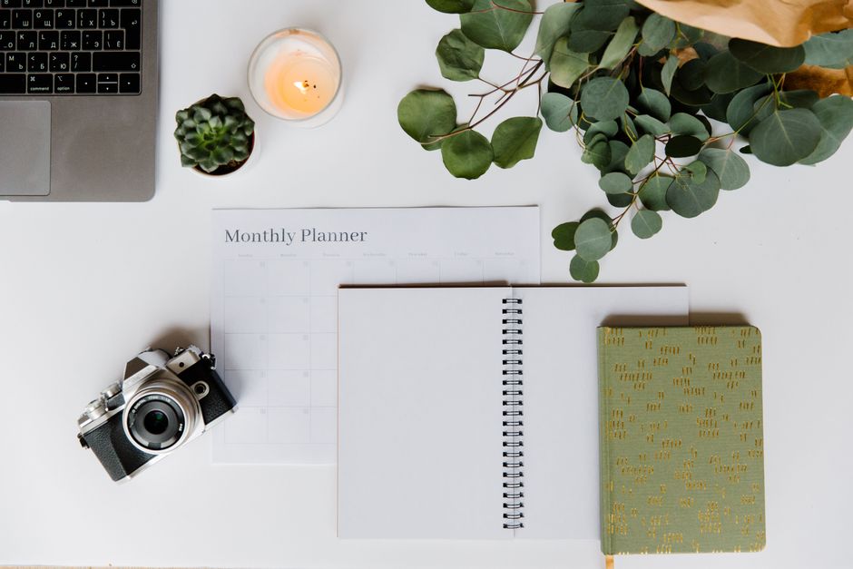 Flat lay of a creative workspace with a planner, analog camera, and laptop for inspiration.