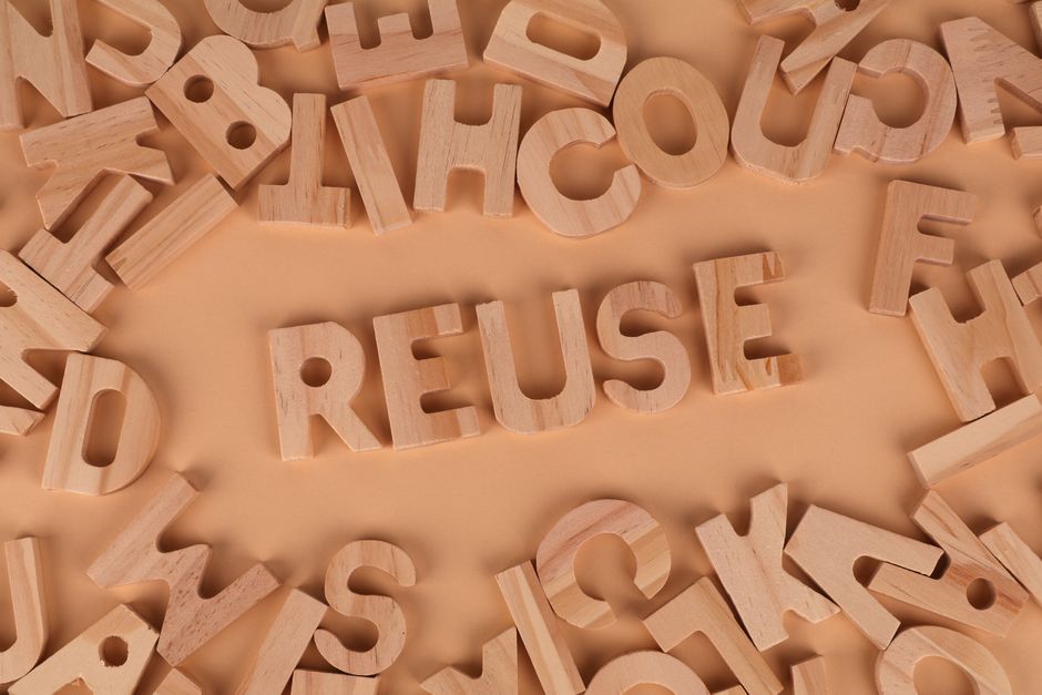 Wooden letters form the word 'Reuse' on a smooth, neutral background, symbolizing sustainability.