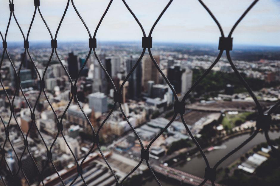 Blurred city skyline view through a chain link fence, creating a sense of depth.