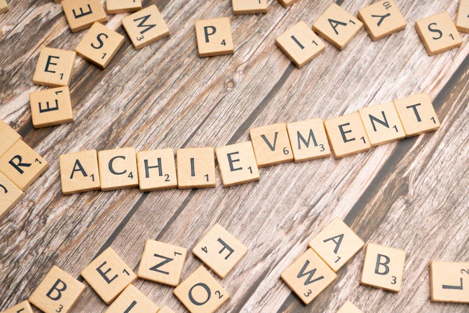 Scrabble tiles spelling 'Achievement' on a wooden surface.