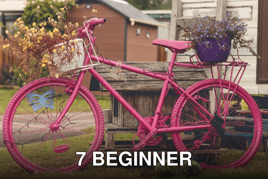 A vibrant pink bicycle adorned with flowering planters set in an outdoor garden area.