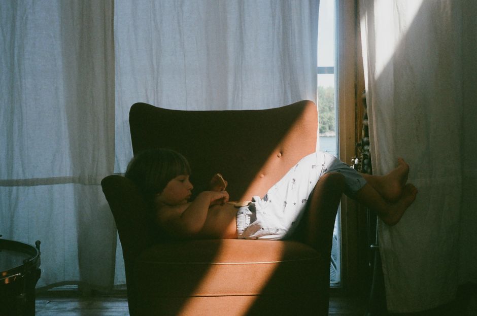 A child relaxing in an armchair with sunlight streaming through a window, creating a warm atmosphere.
