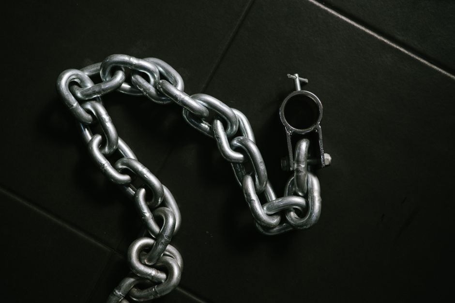 Detailed view of a sturdy metal chain on a dark tile floor, showcasing industrial design.