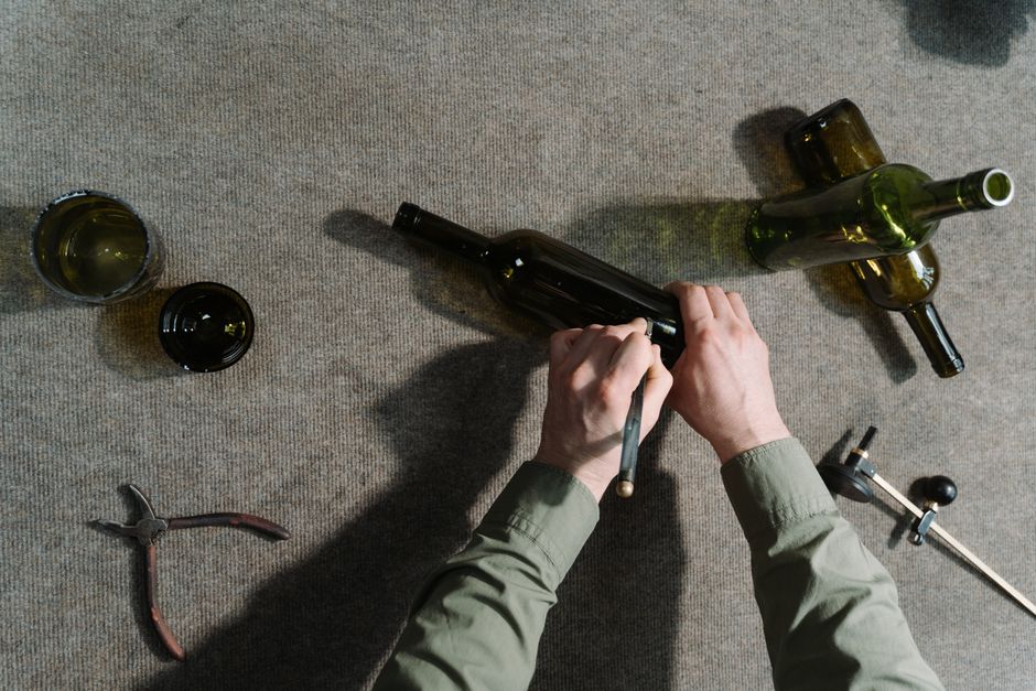 Top view of hands using tools to cut glass bottles, showcasing craftsmanship.