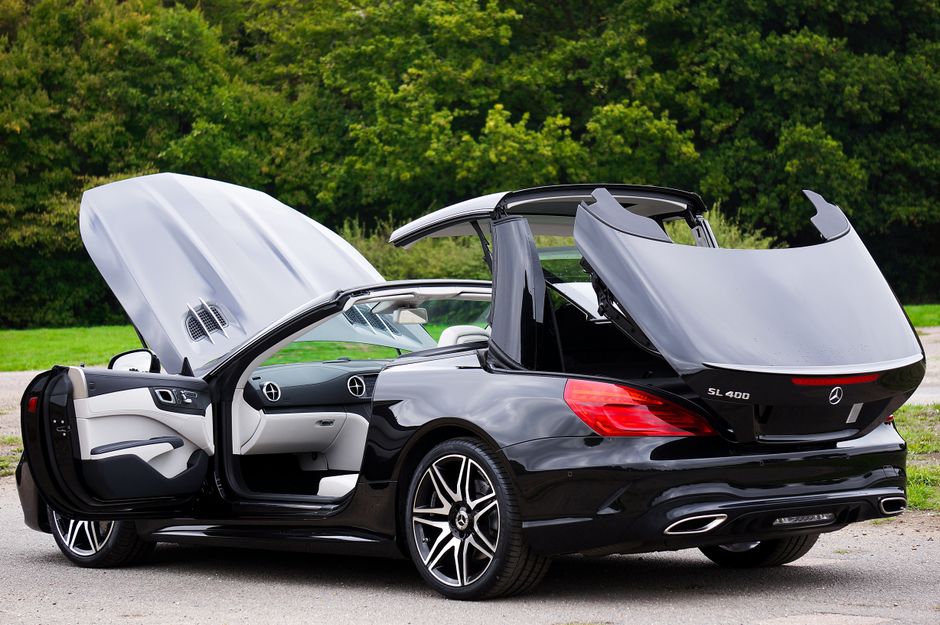 Black luxury convertible car with open roof in a green outdoor setting.