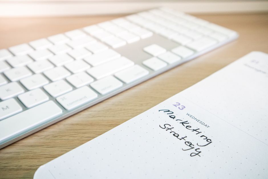 Notebook with marketing strategy note alongside a keyboard on a wooden desk.