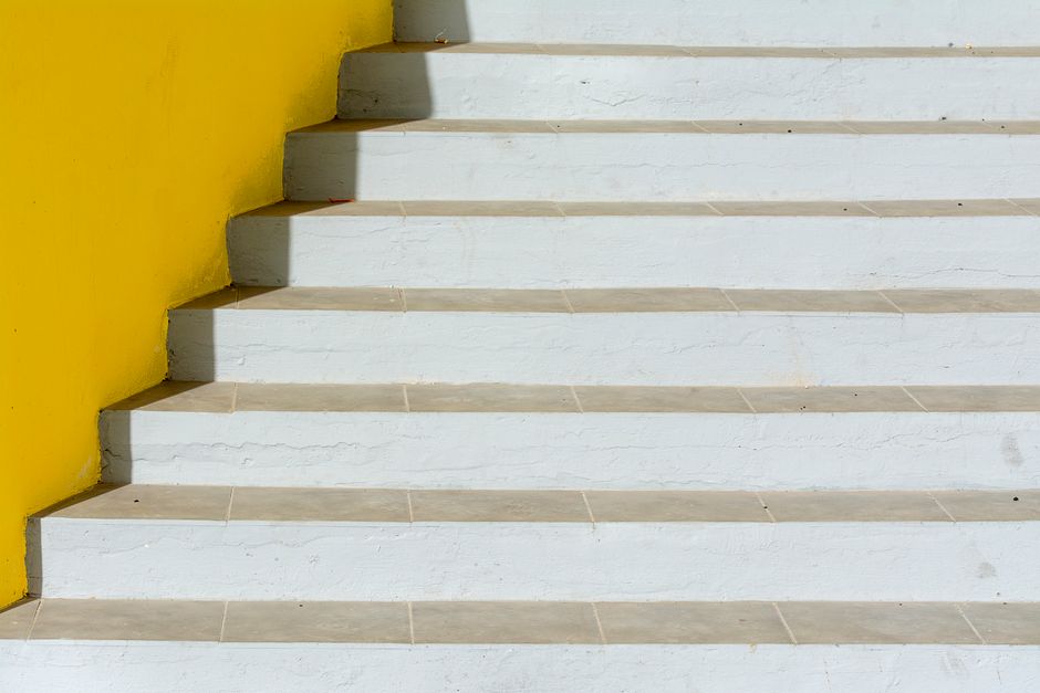 A minimalist staircase with white steps and a vibrant yellow wall. Modern design.