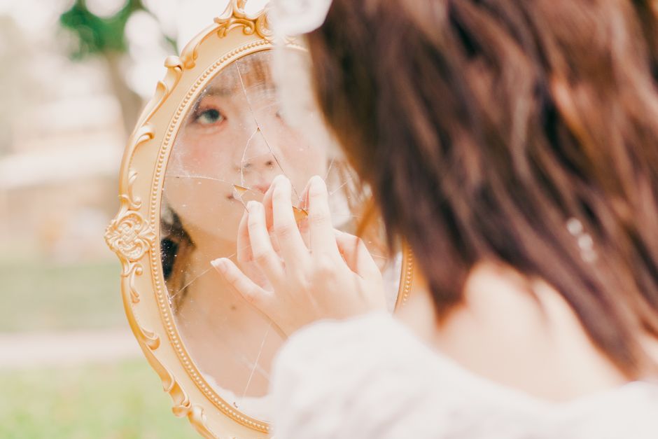 Young woman introspectively touches a broken mirror outdoors in Hanoi, Vietnam.