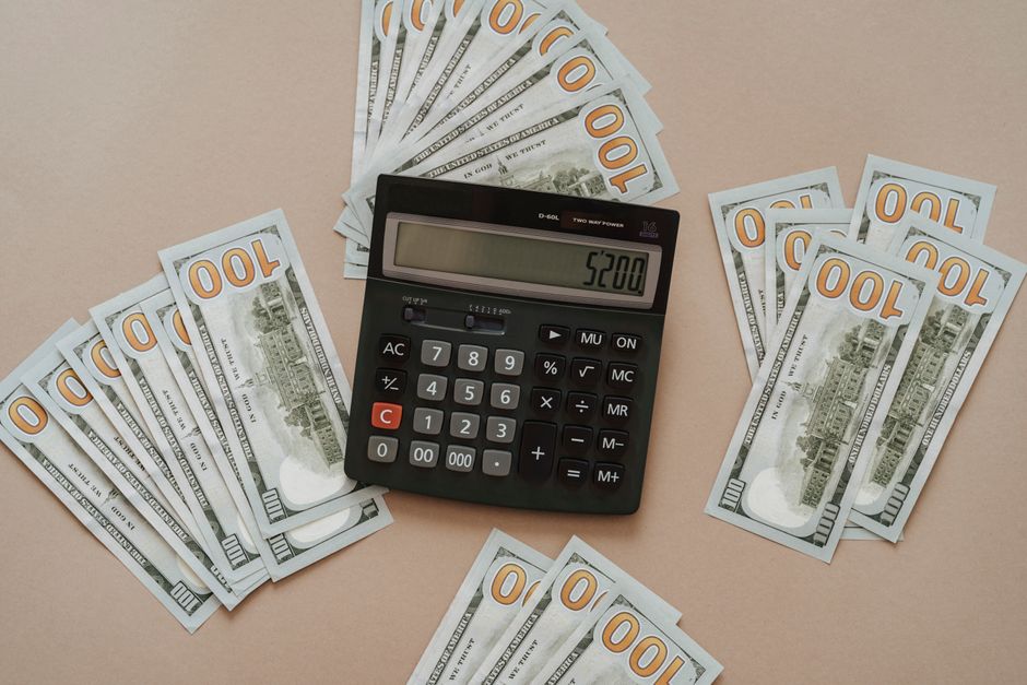 Top view of a calculator showing $5200 surrounded by $100 bills on a tan background.