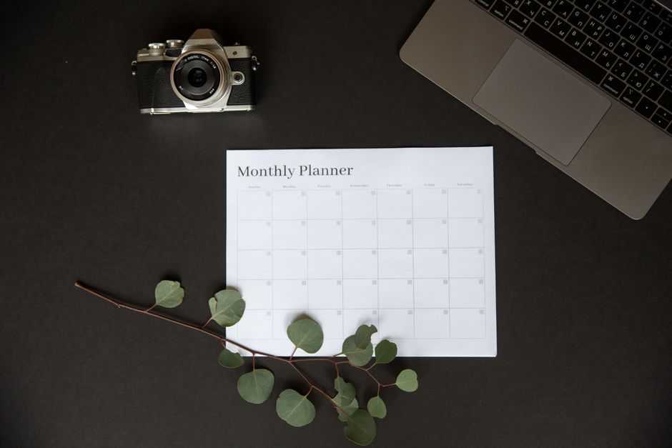 Flat lay of a monthly planner beside a camera and laptop for productivity.