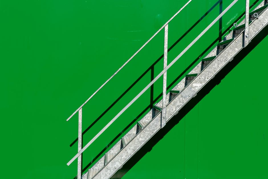 Simple metal staircase contrasting with a vivid green wall in outdoor setting.