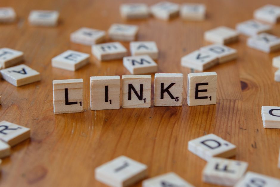 Scrabble tiles arranged to spell 'LINKE' on a wooden table, surrounded by scattered letters.