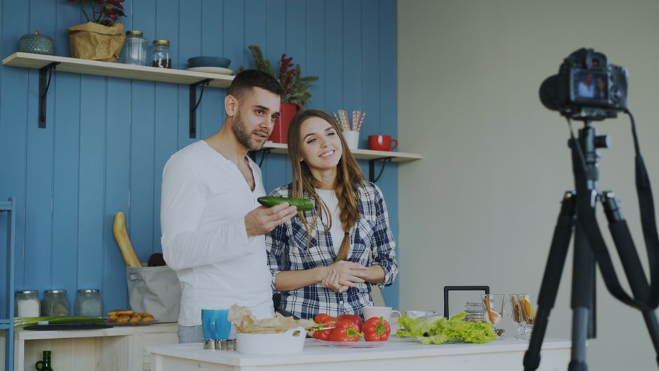 Young couple creating a cooking video in a stylish kitchen setting with fresh ingredients.