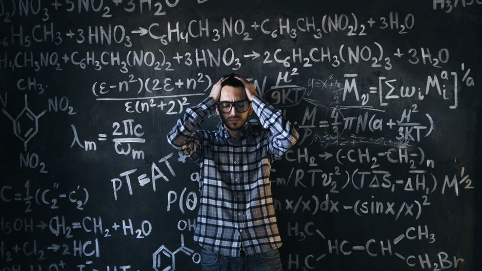 Man in glasses focusing on math problems, struggling with complex equations on chalkboard.