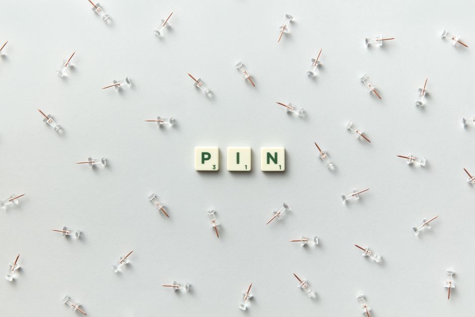 Minimalist arrangement of push pins and scrabble letters spelling 'PIN' on a white background.
