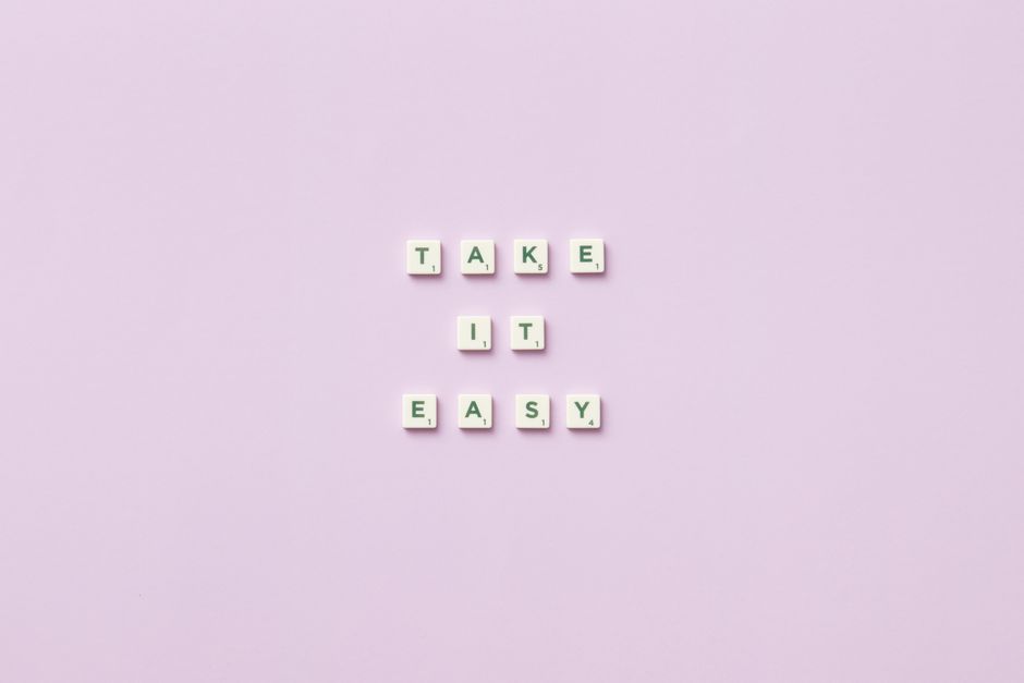 Scrabble tiles forming 'Take it easy' against a soft lilac background, evoking relaxation and mindfulness.