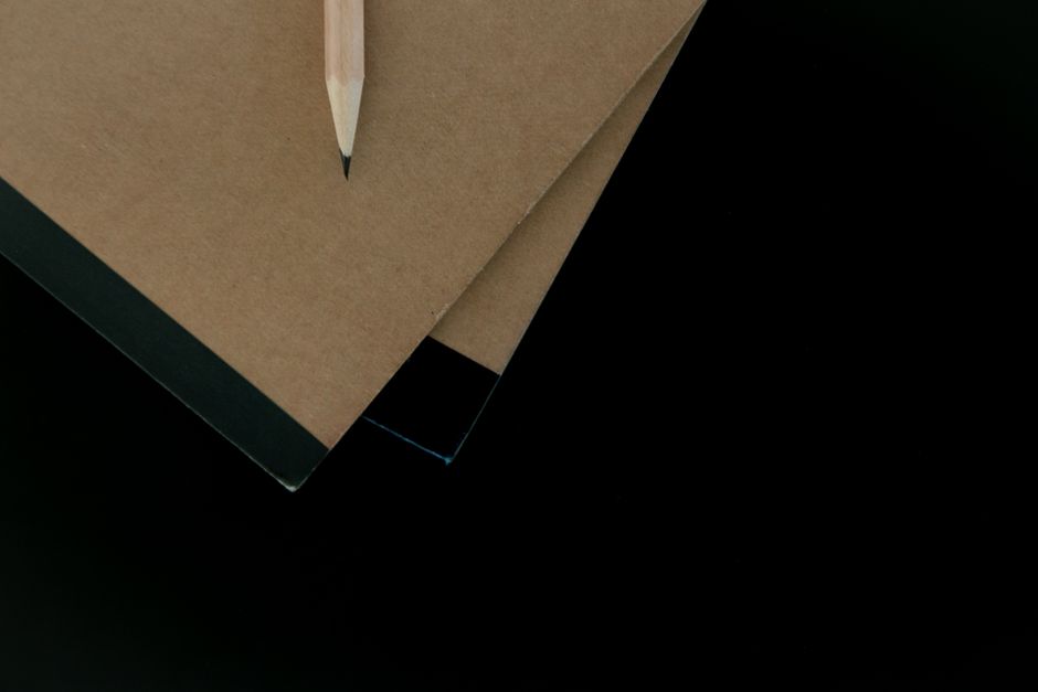 Top view of brown notebooks with a pencil on a black surface, showcasing minimalist design.