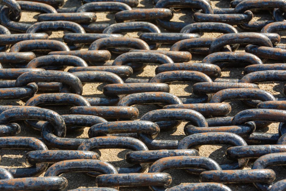 Detailed view of rusty metal chains arranged outdoors in sunlight.