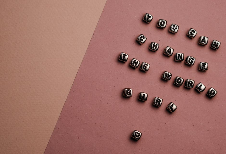 Beaded letter cubes on pink background spell out feminist message: You Can Change the World Girl.