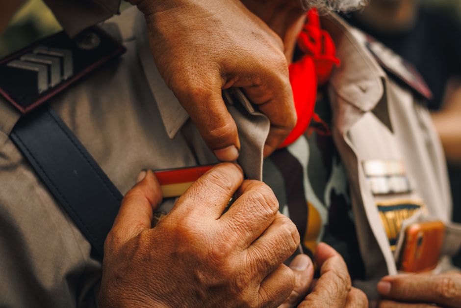 Detailed view of a man adjusting a military uniform with badges and red scarf, signifying readiness.