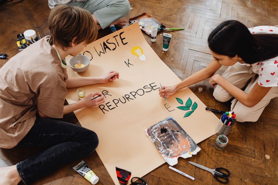 Two teenagers creatively paint a poster promoting eco-friendly practices like recycling and repurposing.