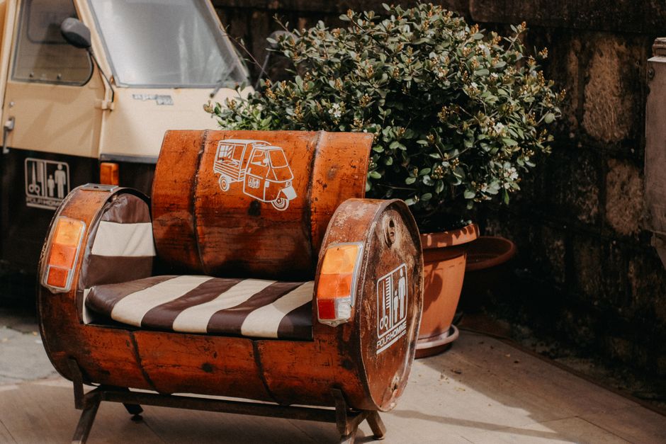 Creative urban armchair made from a recycled barrel and vintage scooter details next to a potted plant.