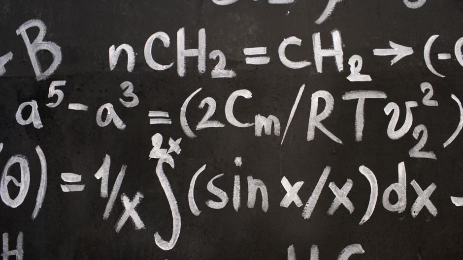 Close-up of complex equations on a chalkboard, showcasing chemistry and math symbols.