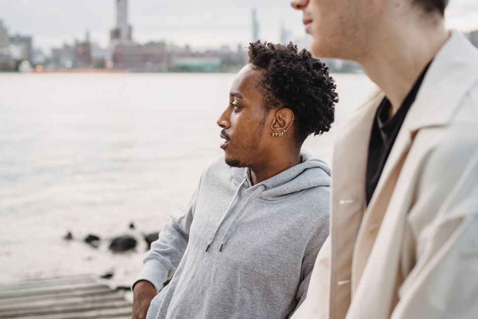 Serious African American male with piercing enjoying view of river standing on shore with friend