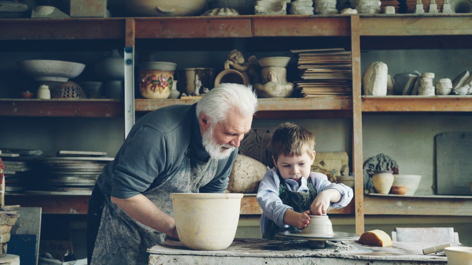 Elderly man and young boy making pottery, highlighting intergenerational learning.