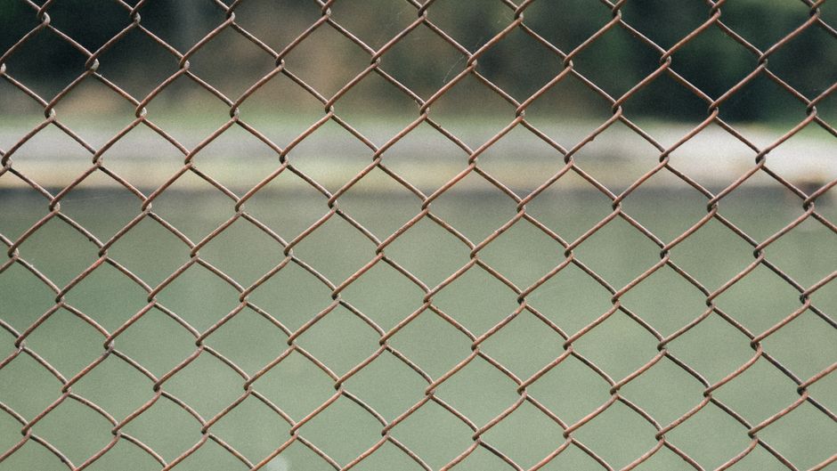 Close-up view of a rusty chain-link fence with blurred background, outdoors.