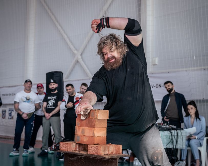 A strongman breaks bricks with his hand at an indoor sports competition event.
