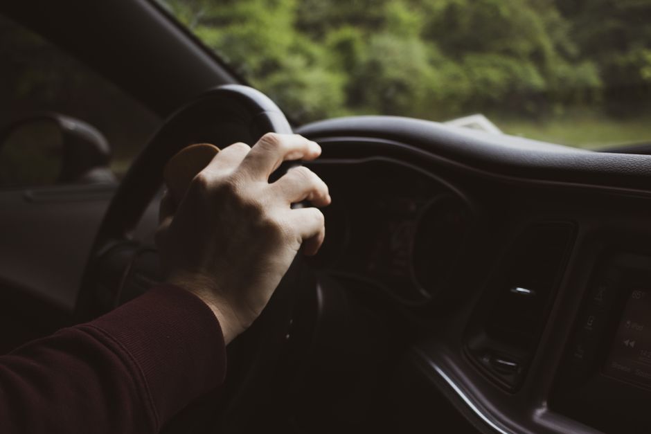 Close-up of a hand on a car steering wheel, depicting a relaxed driving moment.