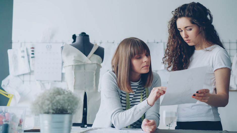 Two fashion designers discussing sketches in a bright studio.