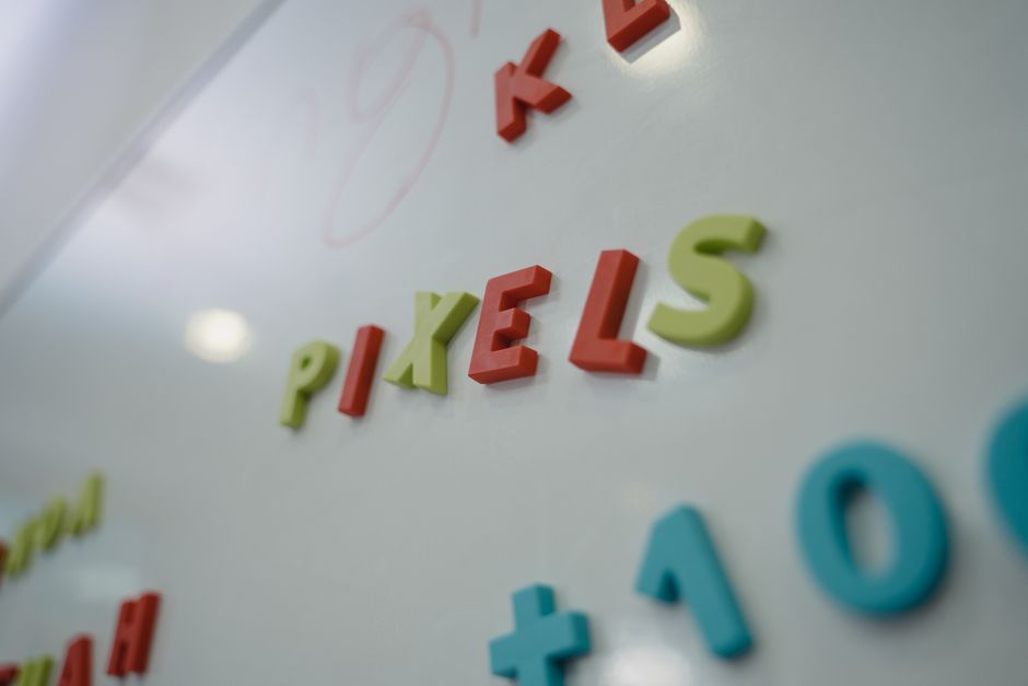 Close-up of colorful magnetic letters spelling 'PIXELS' on a whiteboard.