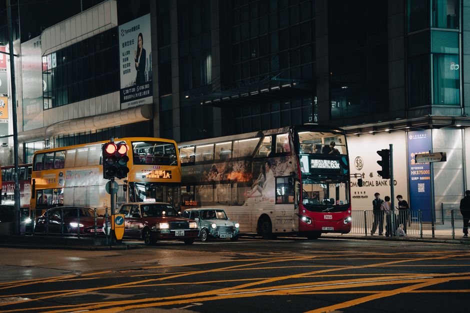 A bustling city street at night with double-decker buses and cars, showcasing lively urban life.