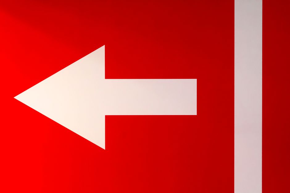 White arrow pointing left on a bold red background, symbolizing direction.