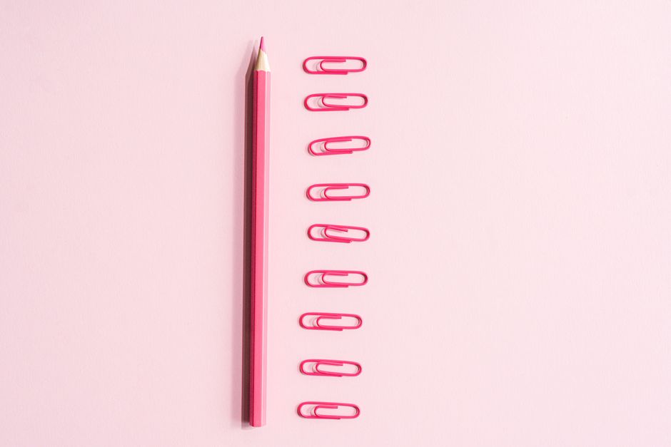 A top view of a pink pencil and pink paper clips arranged neatly on a pastel background.