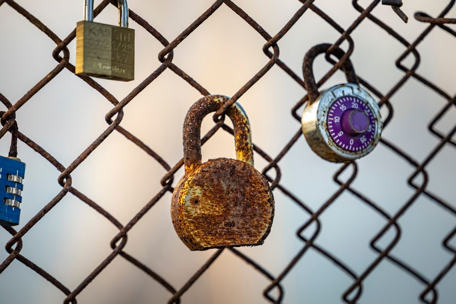 A close-up of a rusty padlock on a chain link fence with additional locks secured, symbolizing security.
