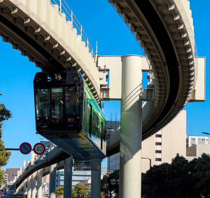 Suspended monorail glides through city's clear sky, showcasing innovative urban transit.