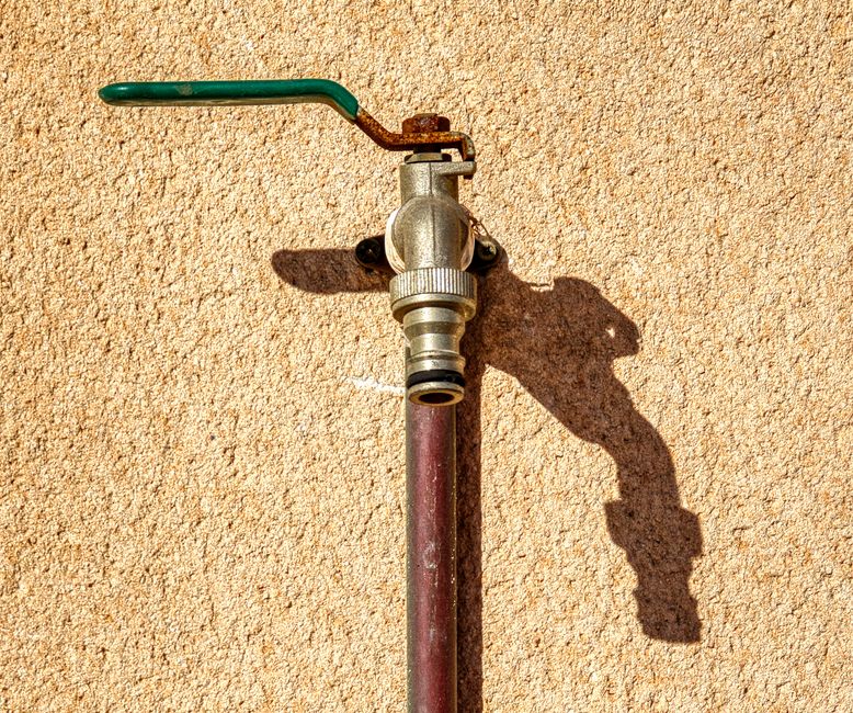 A close-up view of a metal tap on a textured wall casting a shadow.